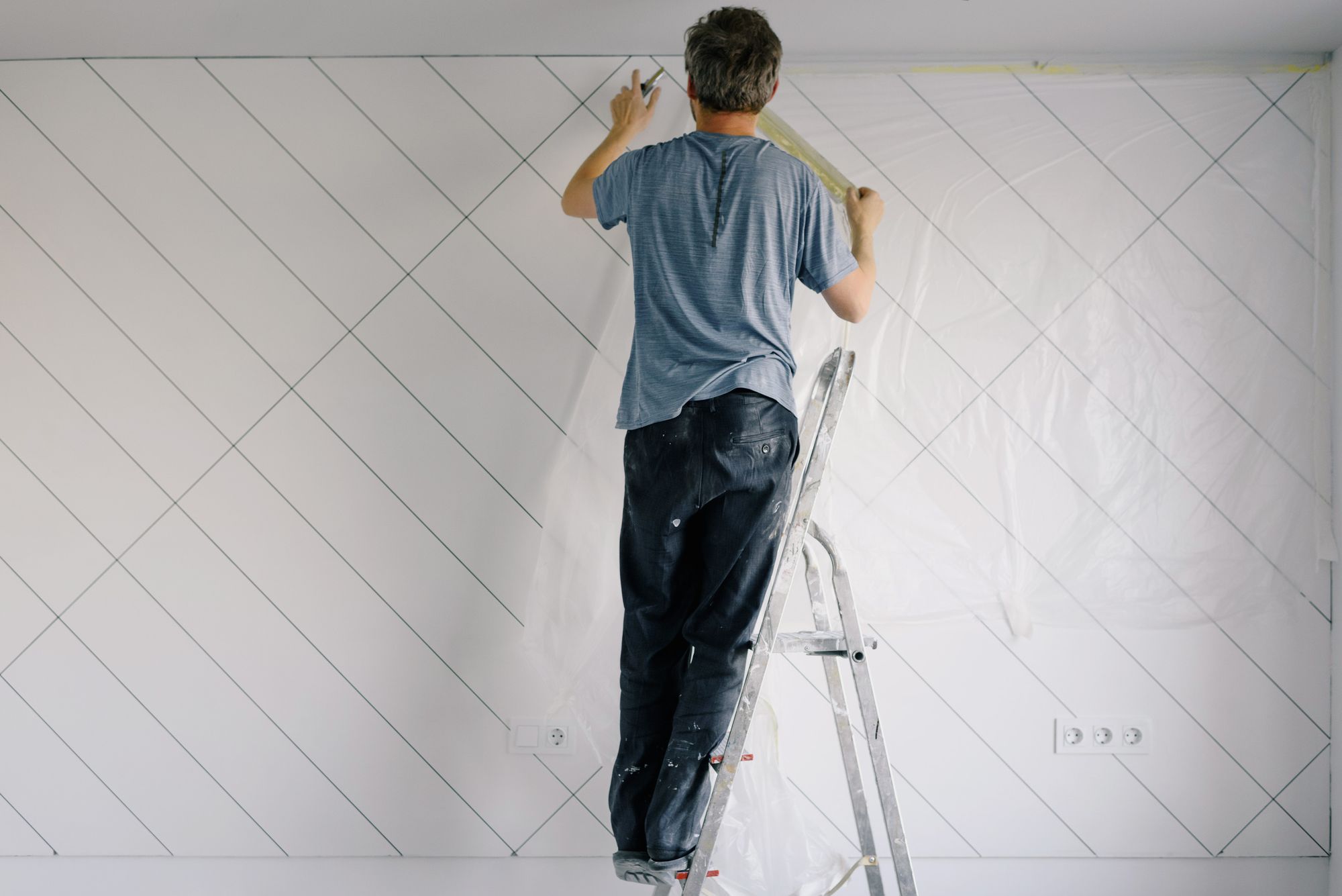 Painter on a ladder taping and painting an interior wall