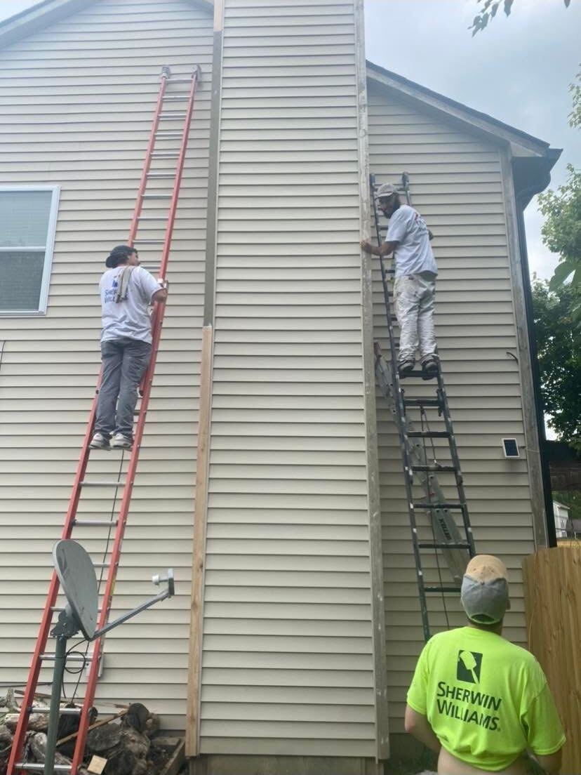 Painters on ladders painting the siding around a chimney