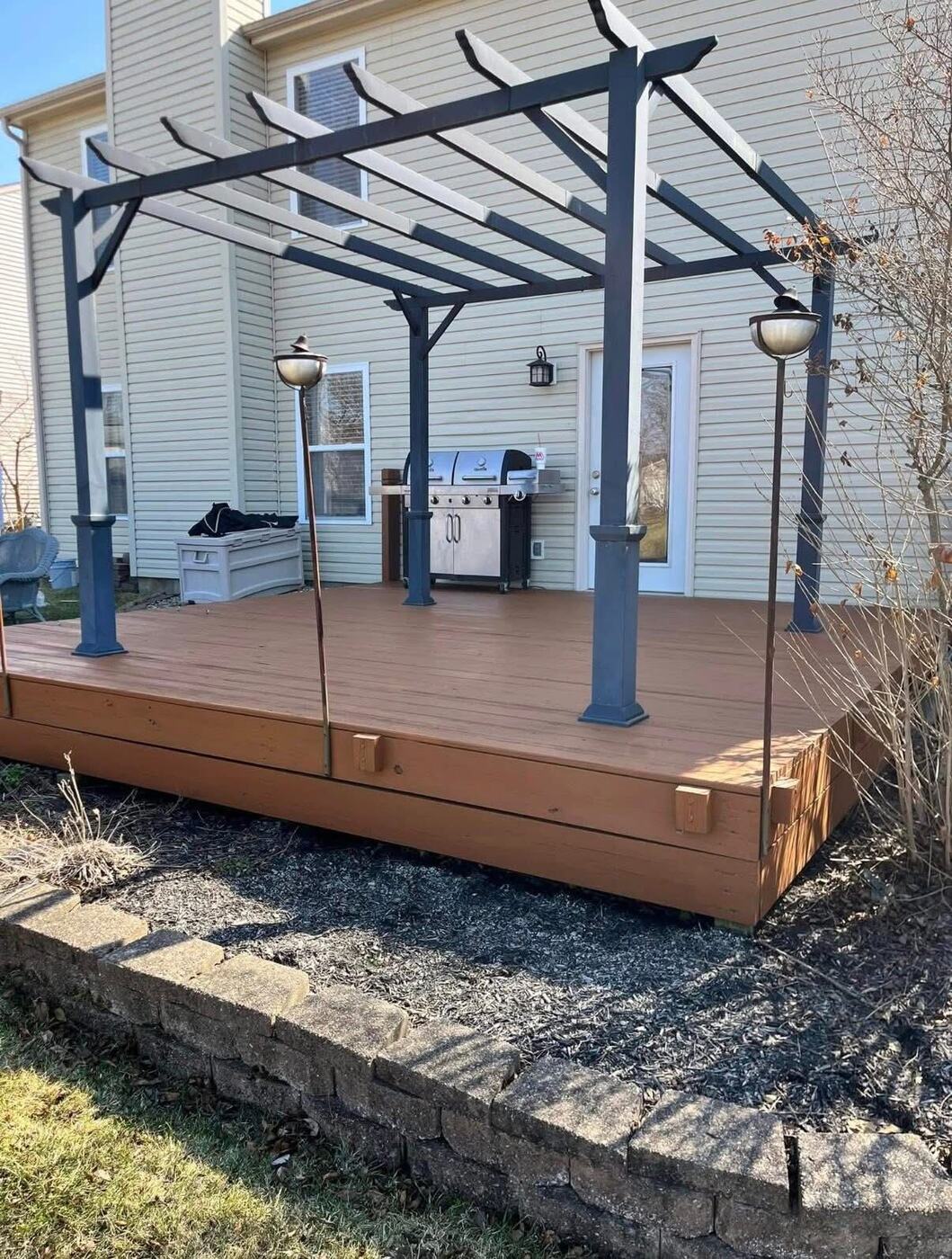 Ground-level deck with fresh stain and a dark painted pergola