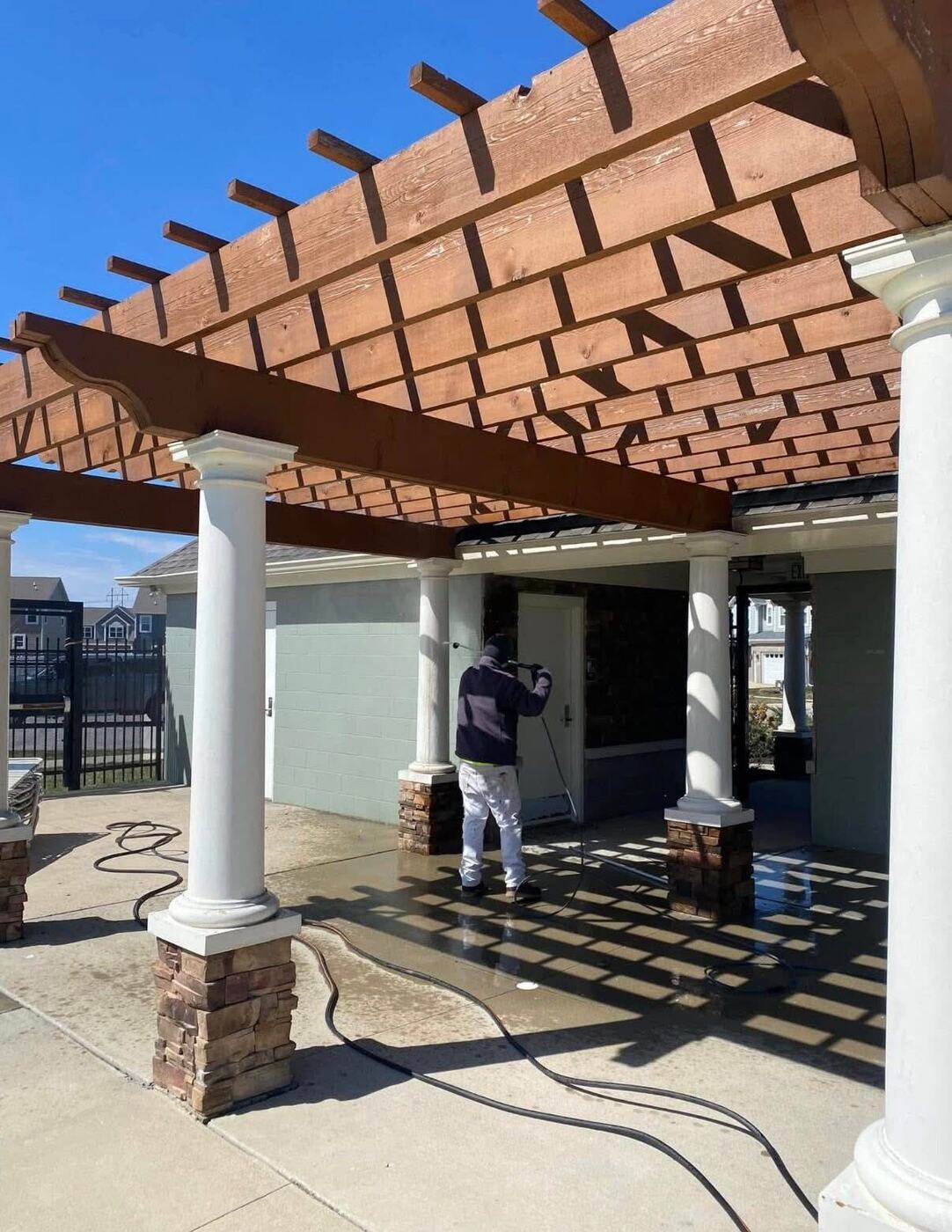 Crew member pressure washing a patio under a wood pergola