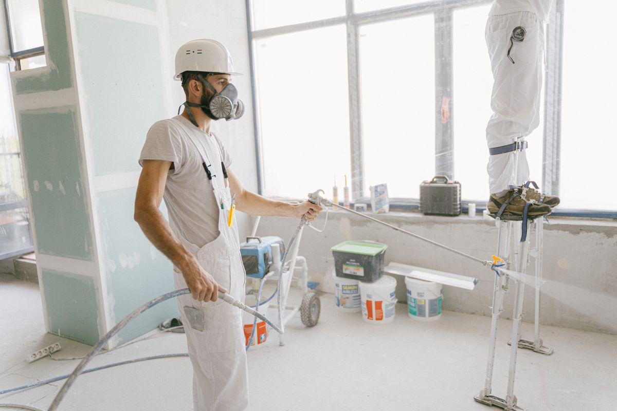 Professional painters in protective gear spray-painting the interior of a large commercial space
